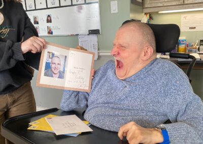 Jim reads a birthday card, smiling, held by a staff member