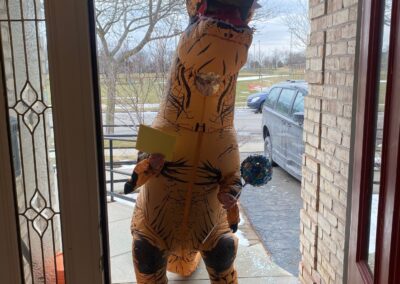 A person in an inflatable dinosaur costume stands in the doorway with a card in hand